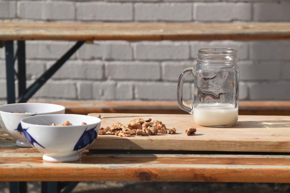 Walnuts beside a glass jar of freshly made homemade nut milk on a wooden board