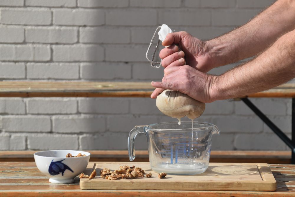 Hands squeezing homemade nut milk through a hemp bag