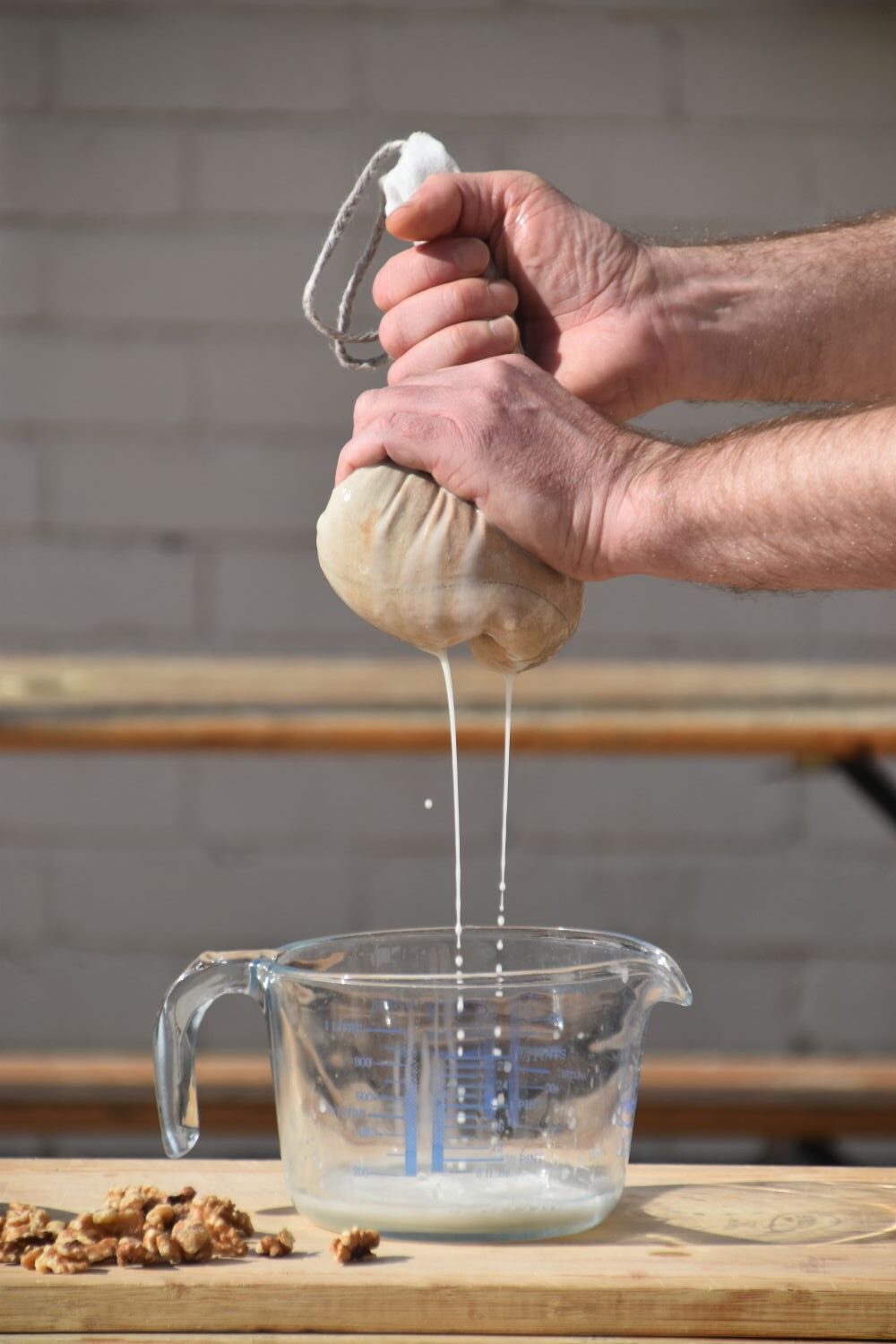 Hands squeezing homemade nut milk through The Nut Sack hemp bag into a glass measuring jug